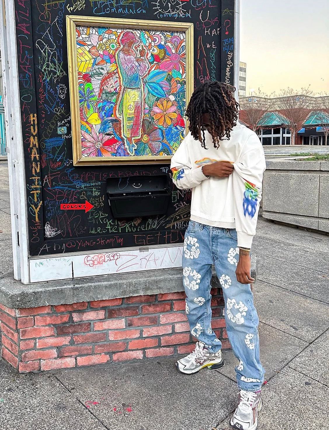 Cream sweater and Denim Tears jeans by a chalk-art mural