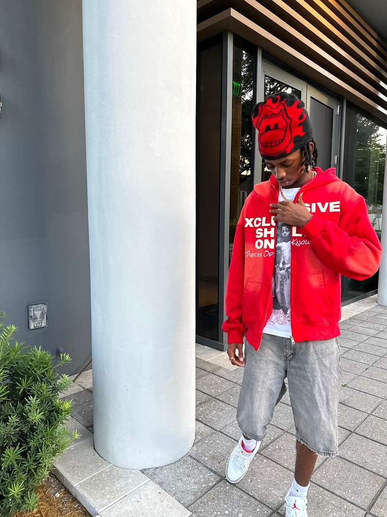 Red Pieces of Knowledge zip-up hoodie beside an exterior column