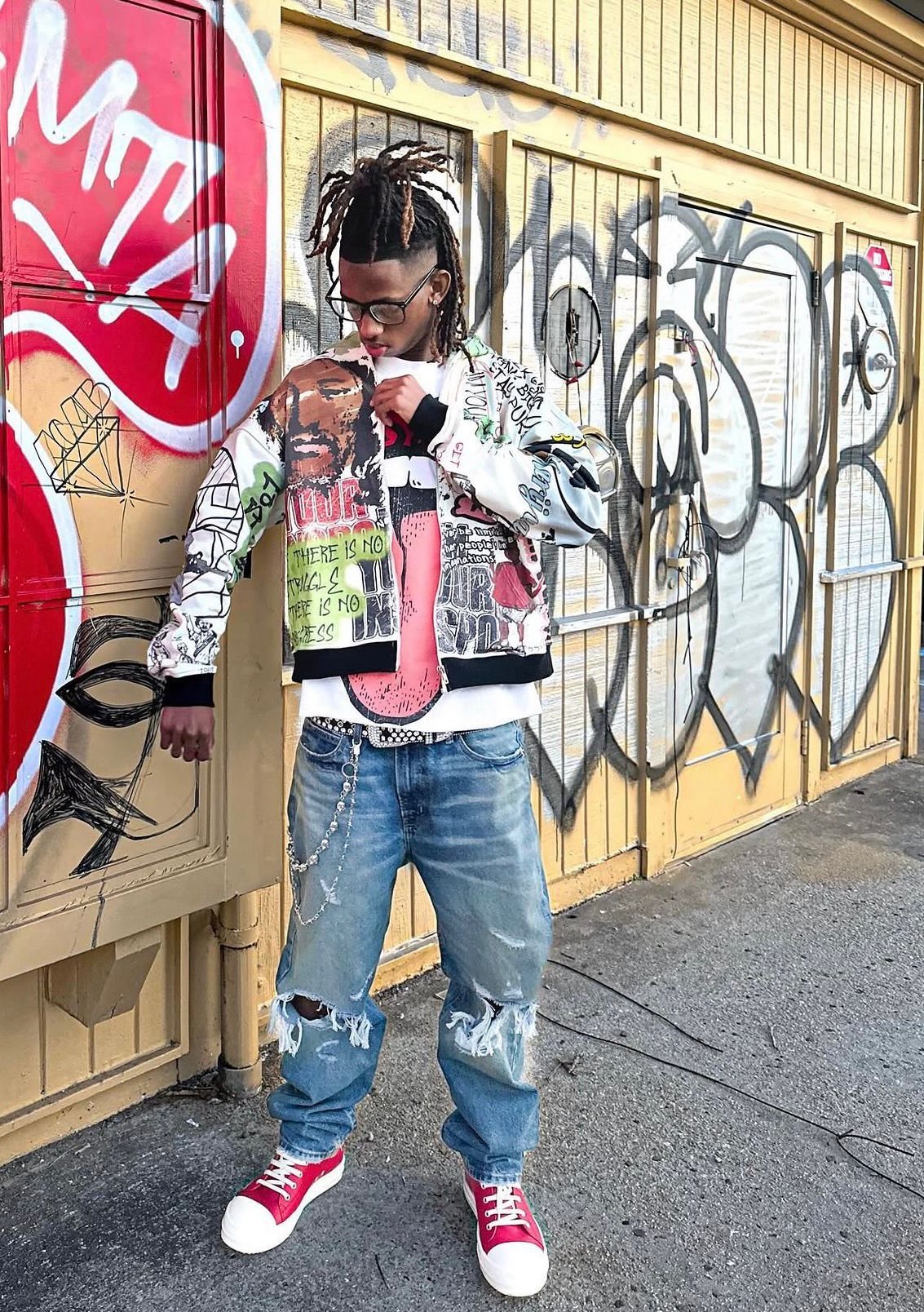 Knowledge Chambers in a graphic bomber jacket against a graffiti wall